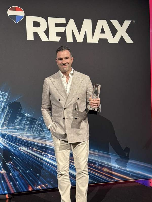 Charles Perreault avec un trophée devant le mur RE/MAX