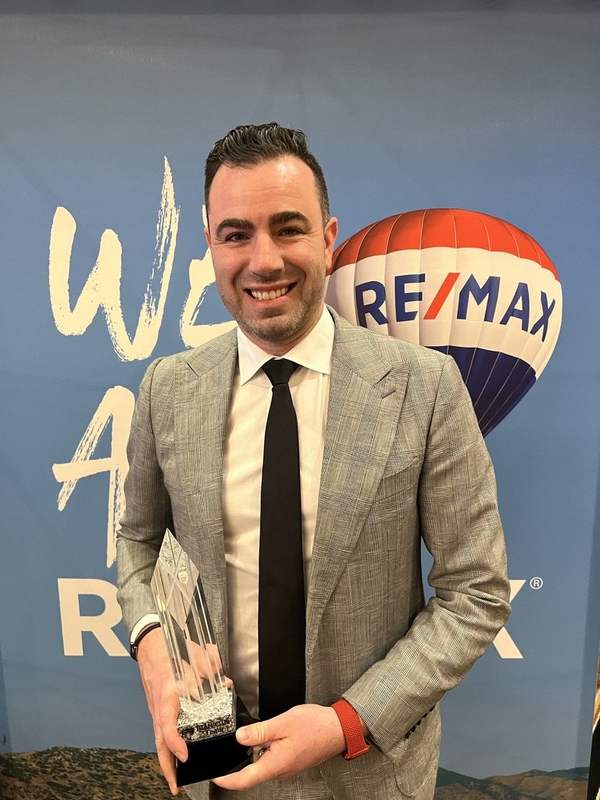 Charles Perreault devant l'affiche We are RE/MAX